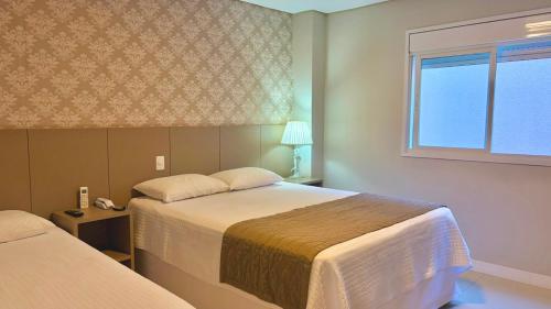 a hotel room with two beds and a window at Hotel Seville Comfort in Telêmaco Borba