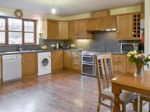 a kitchen with wooden cabinets and a table with a vase of flowers at Elderberry House in Kelly