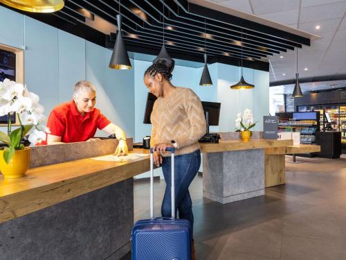 a woman with a suitcase standing at a counter at Ibis Brussels City Centre in Brussels