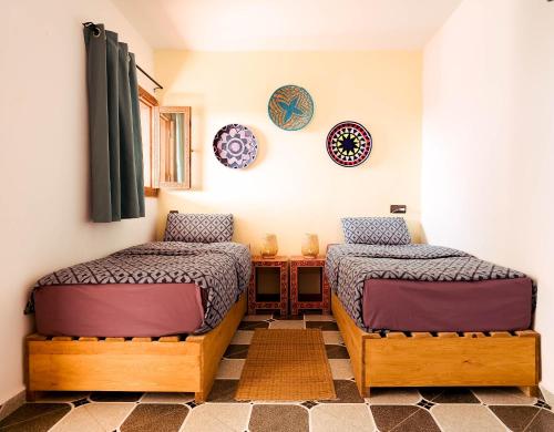 a bedroom with two beds and a table and plates on the wall at Surf hostel Morocco in Tamraght Ouzdar