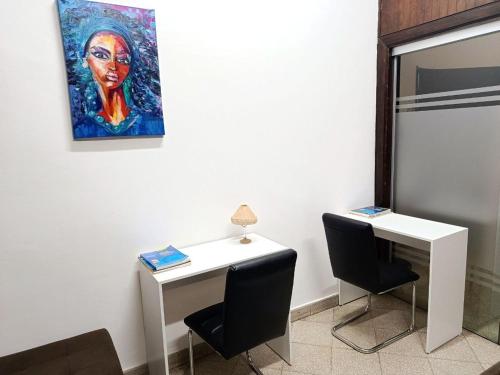 a white desk with two chairs and a painting on the wall at Cuba Linda Capsule Stay in Asunción