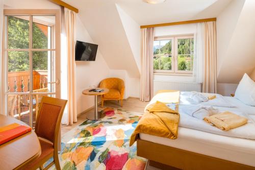 a bedroom with a bed and a desk and a window at Hotel Vitaler Landauerhof in Schladming
