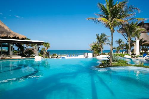 a large swimming pool with palm trees and the ocean at Kore Tulum Retreat & Spa Resort All Inclusive - Adults Only in Tulum