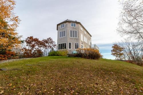 a large house on top of a grassy hill at Bayfront home with 270-degree views, large deck & porch - near Popham Beach in Phippsburg