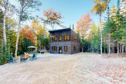 a large wooden house in the woods with chairs at Contemporary retreat with grill, firepit, & patio - walk to beach in Marlboro