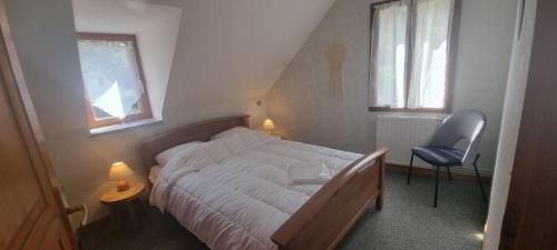 a bedroom with a bed and a chair and two windows at Le logis de l'Ajolaise in Vielle-Aure