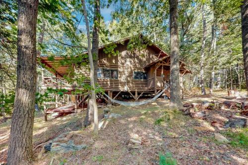 a log cabin in the woods with a hammock in front at Stunning log cabin with fireplace & nature views - near shopping & dining in Boothbay Harbor