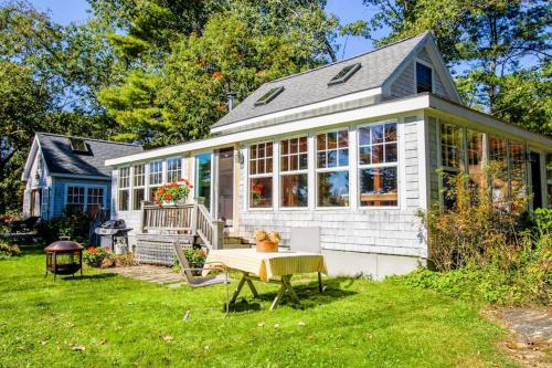 a small white house with a table in the yard at Charming Bayview Cottage with Deck, Firepit, Garden - 200 in East Harpswell