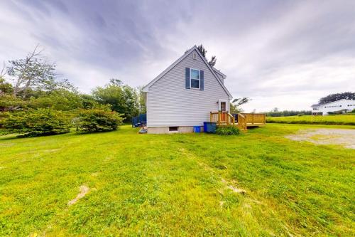 a small white house in a field of grass at Serene home with a deck, grill, firepit, board games, washer/dryer, & mtn views in East Lamoine