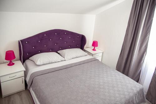 a bedroom with a bed with a purple headboard and two lamps at Apartments Kuc in Tivat