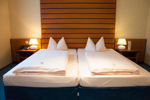 two beds in a hotel room with two lamps at Hotel Stadt Püttlingen in Püttlingen