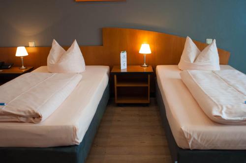 two beds in a hotel room with two lamps at Hotel Stadt Püttlingen in Püttlingen