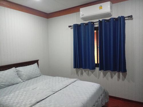 a bedroom with a bed and a window with blue curtains at hadya home in Ko Yao Noi