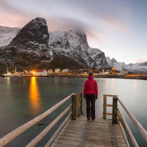 a woman standing on a wooden bridge over a body of water at Valen Cabins in Reine in Reine