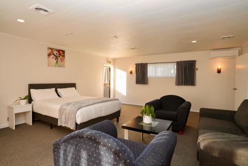 a hotel room with a bed and a couch and chairs at Dukes Midway Lodge in Auckland