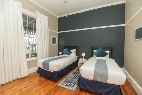 two beds in a room with blue walls and wooden floors at Crown Oak in Gqeberha