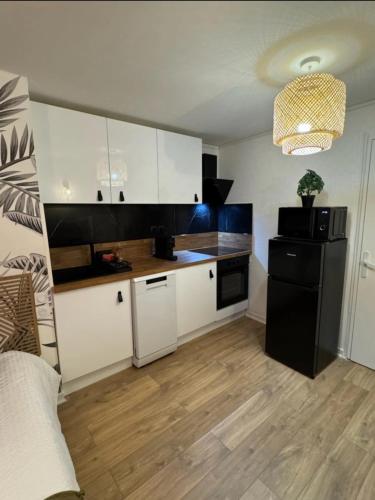 a kitchen with white cabinets and a black refrigerator at Le Nid douillet- Studio Chic au cœur Issoire in Issoire