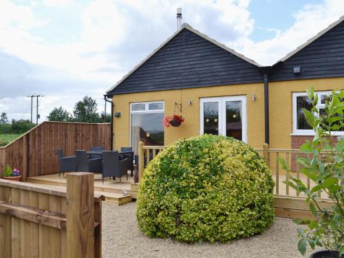 a yellow house with a wooden deck and a fence at Sedge Lodge in Littleport