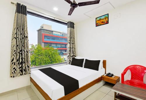 a bedroom with a bed and a window with a red chair at Hotel Kalyan in Rajkot