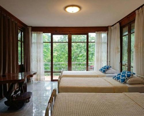 a bedroom with two beds and a table and windows at SN Garden in Ban Bo Hin