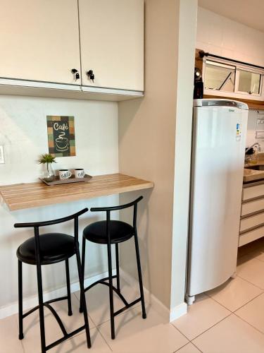 a kitchen with a counter with two stools and a refrigerator at Mandai Apartamentos in Cabo Frio