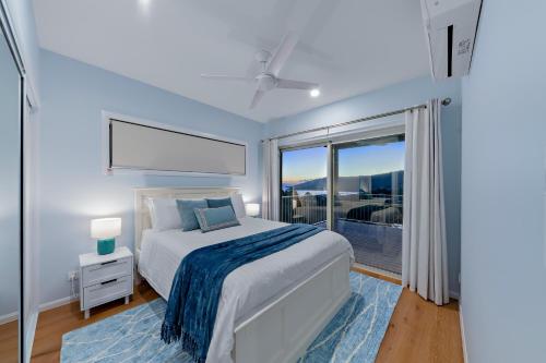 a white bedroom with a bed and a large window at Seabreeze Lookout Azul in Airlie Beach