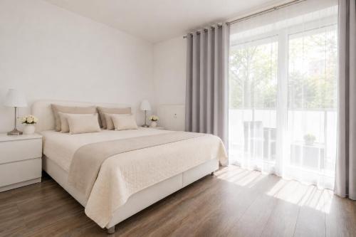 a white bedroom with a large bed and a large window at ALURE RESIDENCES 1 & 24h self check-in, free parking in front of the apartment building, new building, terrace, cafe with breakfast in the apartment building, next to the aqua park in Banská Bystrica