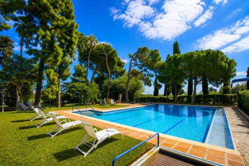 a swimming pool in a park with chairs and trees at Villa COLONIAL in Vilaseca de Solcina