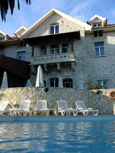 a house with a row of chairs next to a pool at Hotel Solar Palmeiras in Paço de Arcos