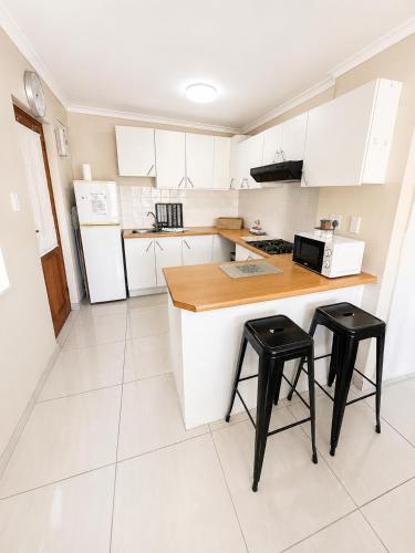 a kitchen with white cabinets and black stools at Unit 5 in Serengeti Complex, Bloemhof, Bellville in Blomtuin