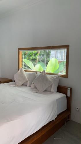 a bed with white pillows and a large window at my house guest house in batumadeg