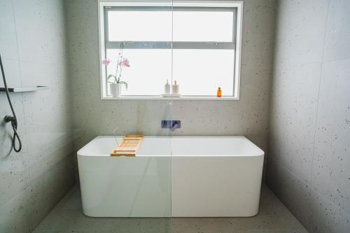 a white bathroom with a tub under a window at Southern Peaks - Private Room in Queenstown Airport
