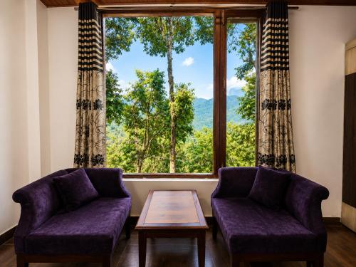 a living room with two chairs and a table and a large window at Kavin Highland - The Mall Dalhousie in Dalhousie