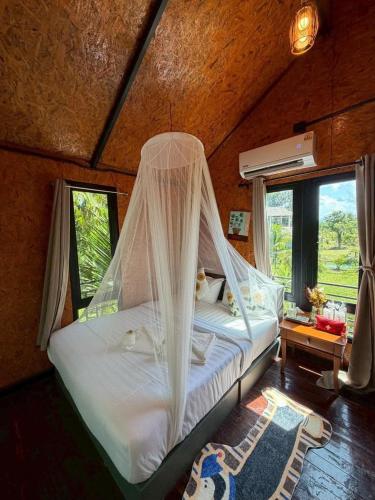 a bed with mosquito net in a room with windows at ภูธาราทรีเฮาส์แอทเชี่ยวหลาน Phutara Treehouses At Cheowlan in Ban Pha Saeng Lang