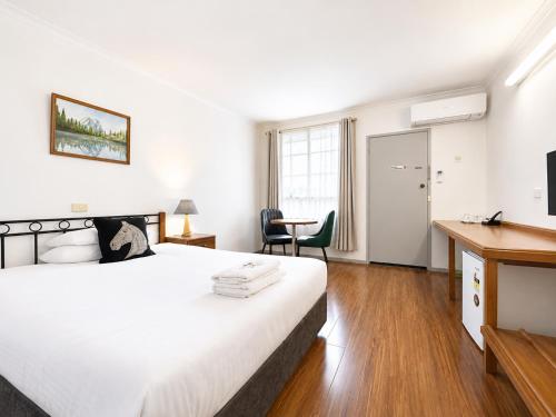 a bedroom with a large white bed and a desk at Beaconsfield Lodge Motel in Beaconsfield