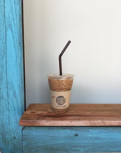 a cup of coffee with a straw on a wooden table at The Rhea in Udon Thani