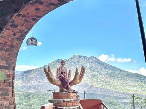 Caldera Hotel & Restaurant في Kintamani: امرأة تجلس على تمثال أمام جبل