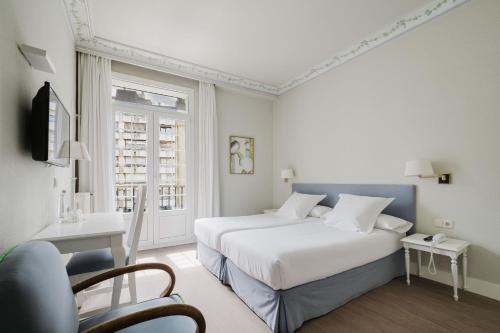 a white bedroom with a bed and a chair at Hotel Niza in San Sebastián