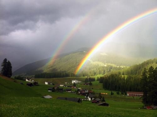 a rainbow over a green field with a town at BnB Guesthouse Lusi in Frauenkirch