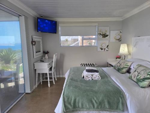 a bedroom with a bed and a desk and a television at View on 42 - Protea Room - Small cozy room with ocean view in Mossel Bay