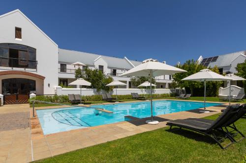 a swimming pool with chairs and umbrellas in front of a building at Winelands Golf Lodges 28 in Stellenbosch