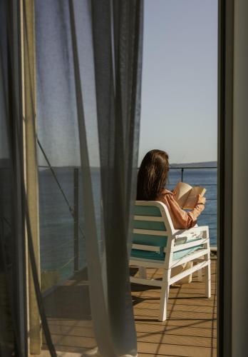 a woman sitting in a chair reading a book on a balcony at Hotel Štacija in Kaštela