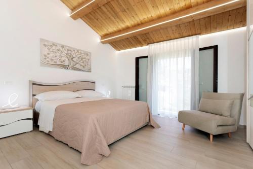 a white bedroom with a bed and a chair at Perla Dell'Etna Holiday House in Zafferana Etnea