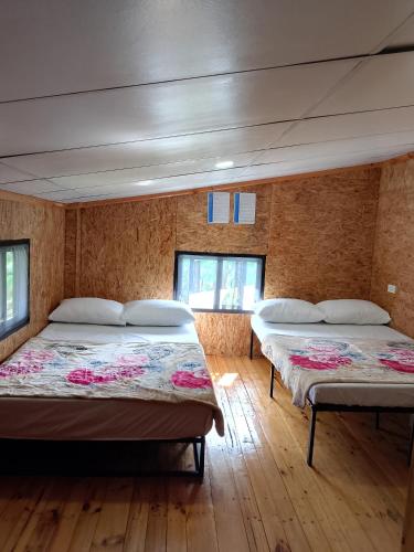 two beds in a room with wooden floors and windows at Gia's Baguio Transient House in Baguio