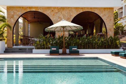 a pool with chairs and an umbrella next to a building at Kanalla Boutique Hotel - Adults Only in Kuta Lombok
