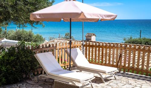 two chairs and an umbrella on a patio with the ocean at Corfu Dream Holidays Villas in Glyfada