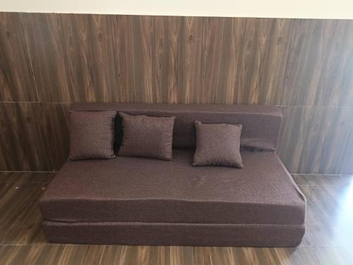 a couch with three pillows sitting on a wooden floor at Ira's Abode in Dibrugarh