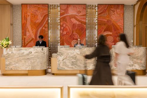 a woman walking through a lobby with two people in a room at Amora Hotel Adelaide in Adelaide