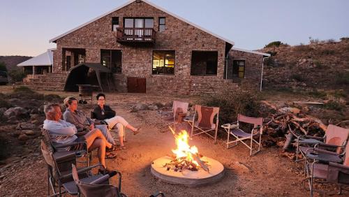 a group of people sitting around a fire in front of a house at Shama Private Group Lodge in Steytlerville