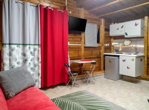 a living room with a red curtain and a kitchen at Maison cosy avec piscine partagée à Capesterre-Belle-Eau in Besnard